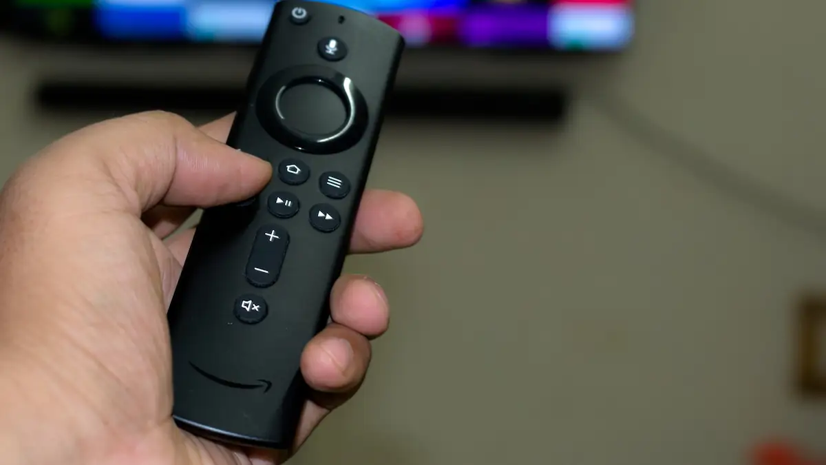 Amazon Fire TV Stick Fernbedienung in einer Hand auf einen Fernseher gerichtet