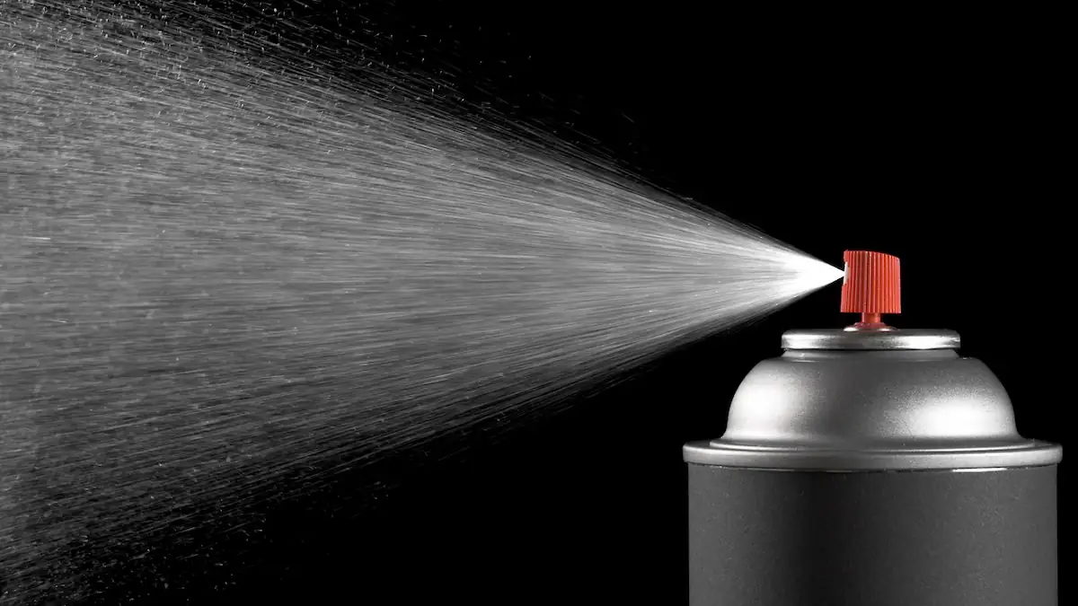 Dusting Symbolbild: Sprühkopf einer Dose in Aktion vor schwarzem Hintergrund