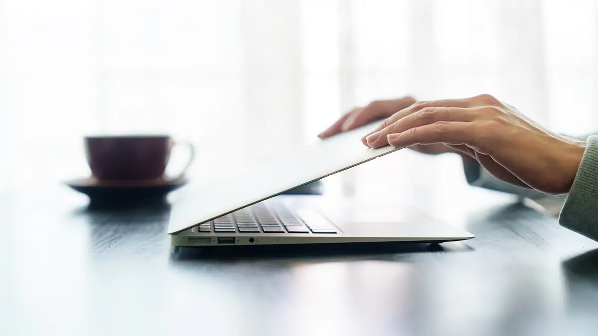 Jemand schließt einen Laptop neben einer Kaffeetasse