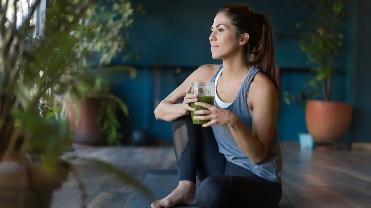 Sirt Diät: Porträt einer fitten lateinamerikanischen Frau, die im Fitnessstudio einen grünen Detox-Smoothie trinkt