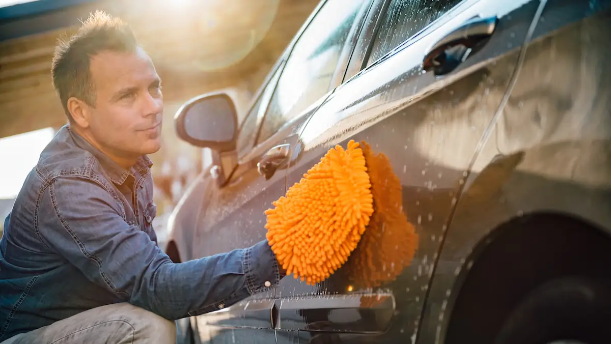 Mann beim Auto waschen mit oragenem Lappen