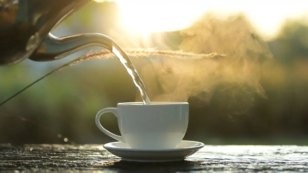 Dampfende heiße Tasse in der Sonne, dazu schenkt eine Kanne weiter ein