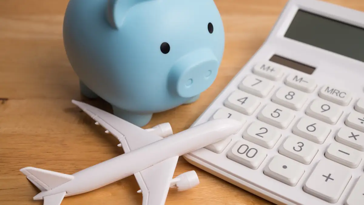 Urlaub: Taschenrechner liegt neben Sparschwein und einem Flugzeug-Modell