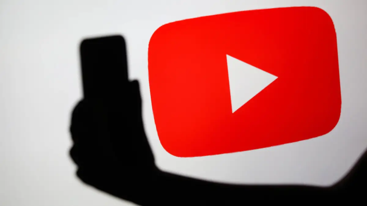 YouTube Logo auf weißem Grund, davor die Silhouette einer Hand mit Handy