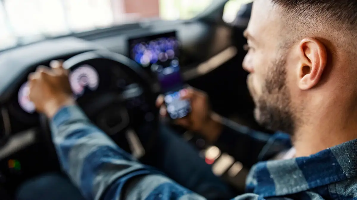 Mann fährt Auto, im Hintergrund sind Infotainment-Systeme zu sehen