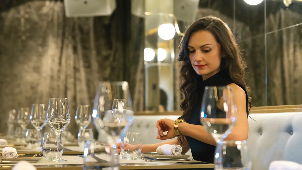 Double Seating Symbolbild: Frau schaut im Restaurant auf ihre Armbanduhr