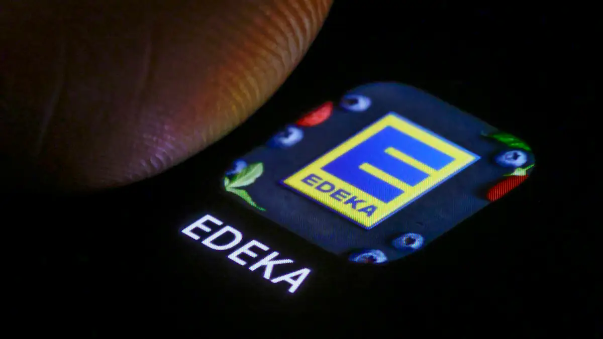 Das Logo der EDEKA App ist neben einem Finger auf einem Smartphone zu sehen. Berlin, 03.01.2025.