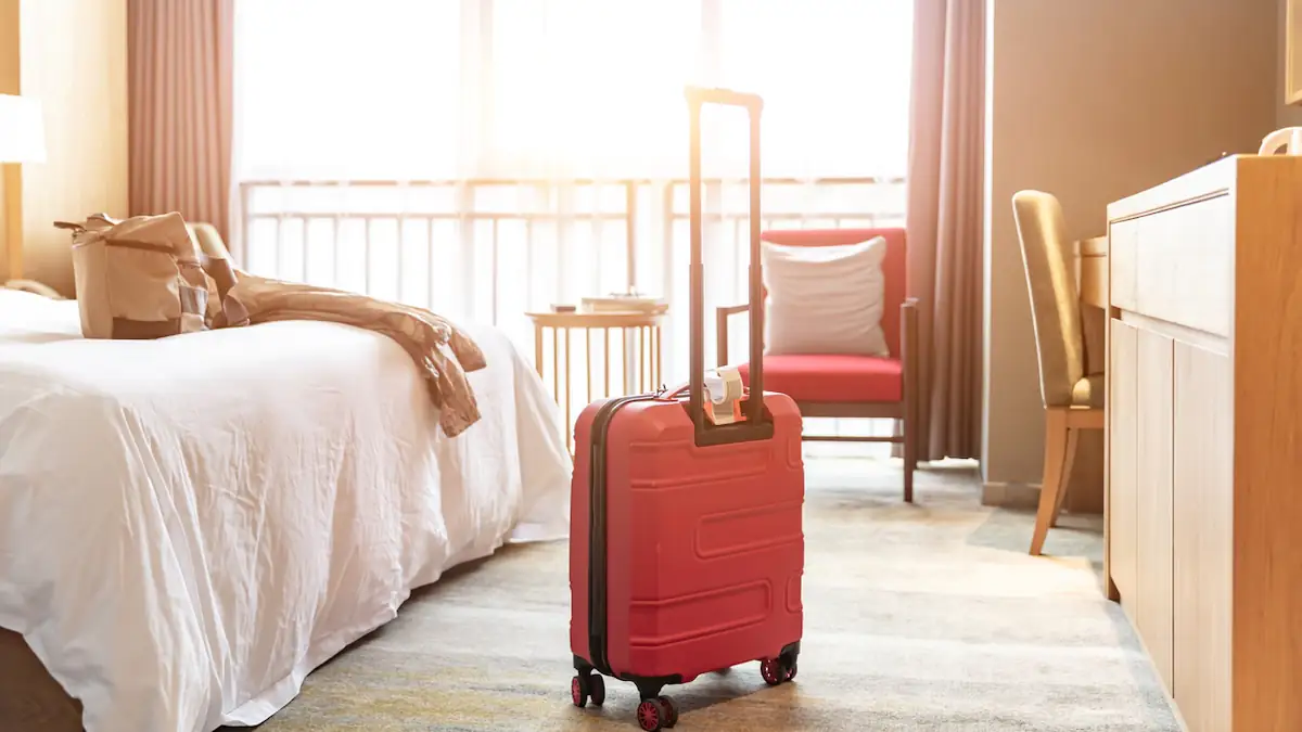 Hotelbuchung: Roter Koffer steht in einem Hotelzimmer