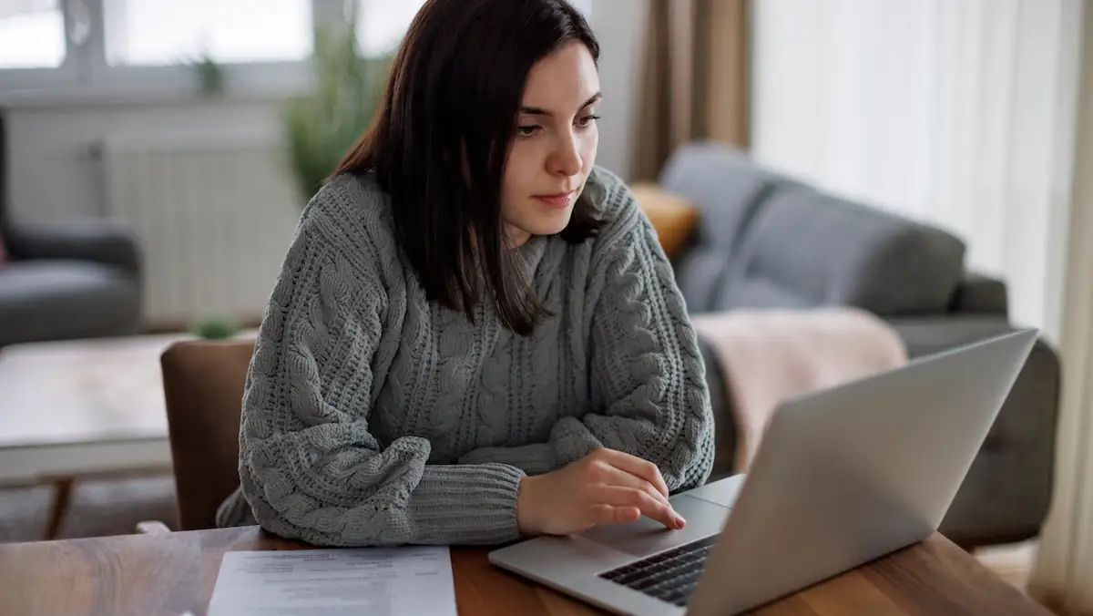 Jobsuche Betrug Symbolbild: Junge Frau mit ihrem Lebenslauf sitzt vor einem Laptop