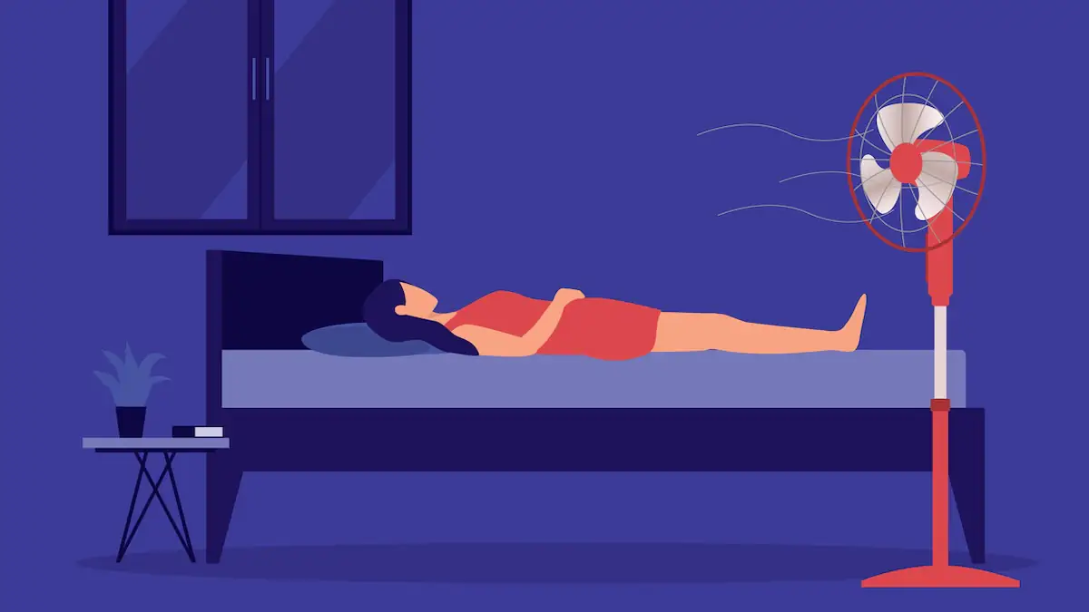 Eine Frau schläft ohne Decke auf dem Bett, während ein elektrischer Standventilator direkt auf sie bläst. Isoliert auf farbigem Hintergrund.