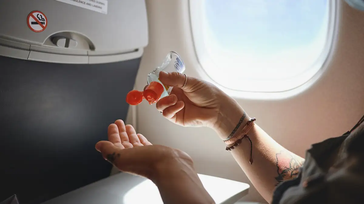 Frau desinfiziert sich im Flugzeug mit einer kleinen Flasche die Hände