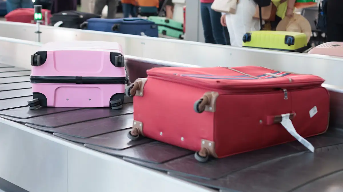Ein roter und ein rosaner Koffer liegen mit Etikett nebeneinander auf dem Gepäckband