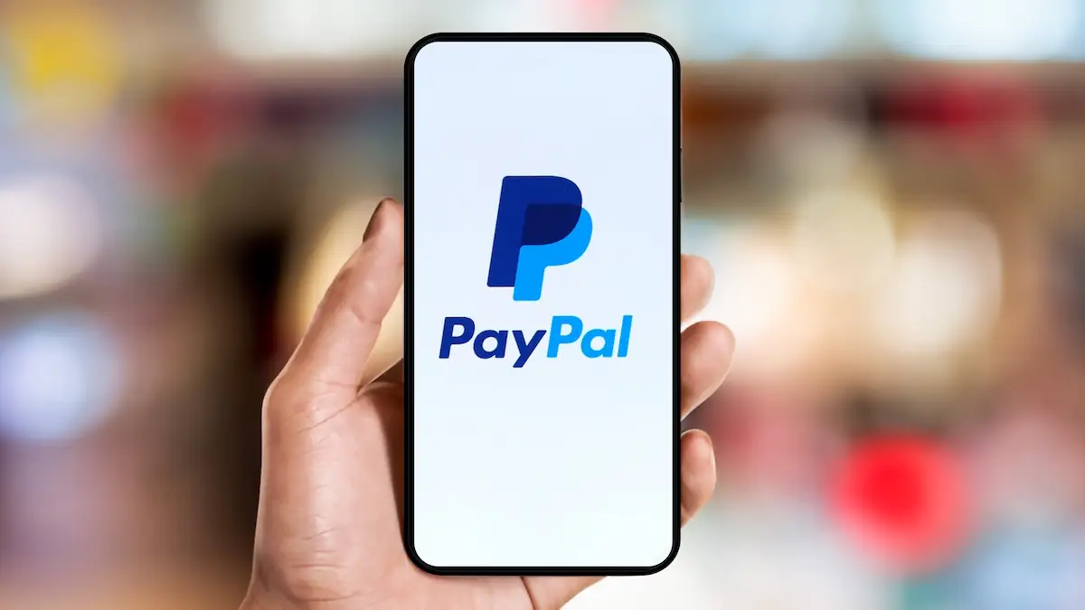 PayPal-Logo und Schriftzug auf einem Smartphone, das jemand in der Hand hält