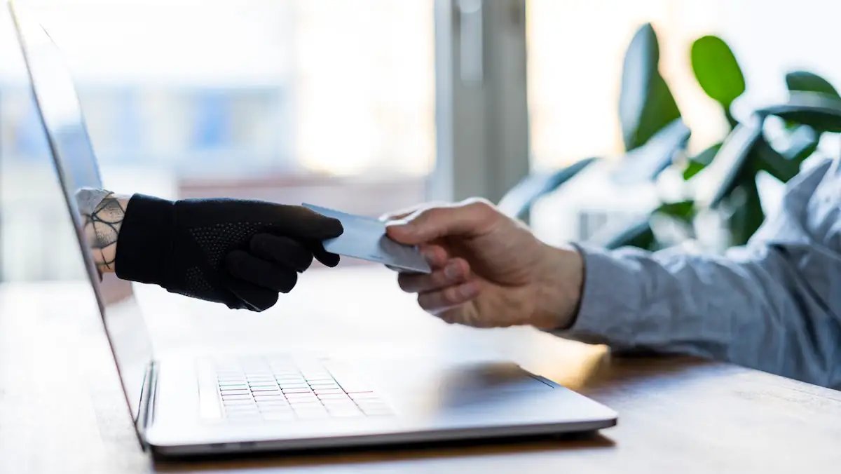 Betrug zum Prime Day Symbolbild: Behandschuhte Hand eines HAckers greift durch einen Bildschirm hindurch nach der Kreditkarte eines Opfers