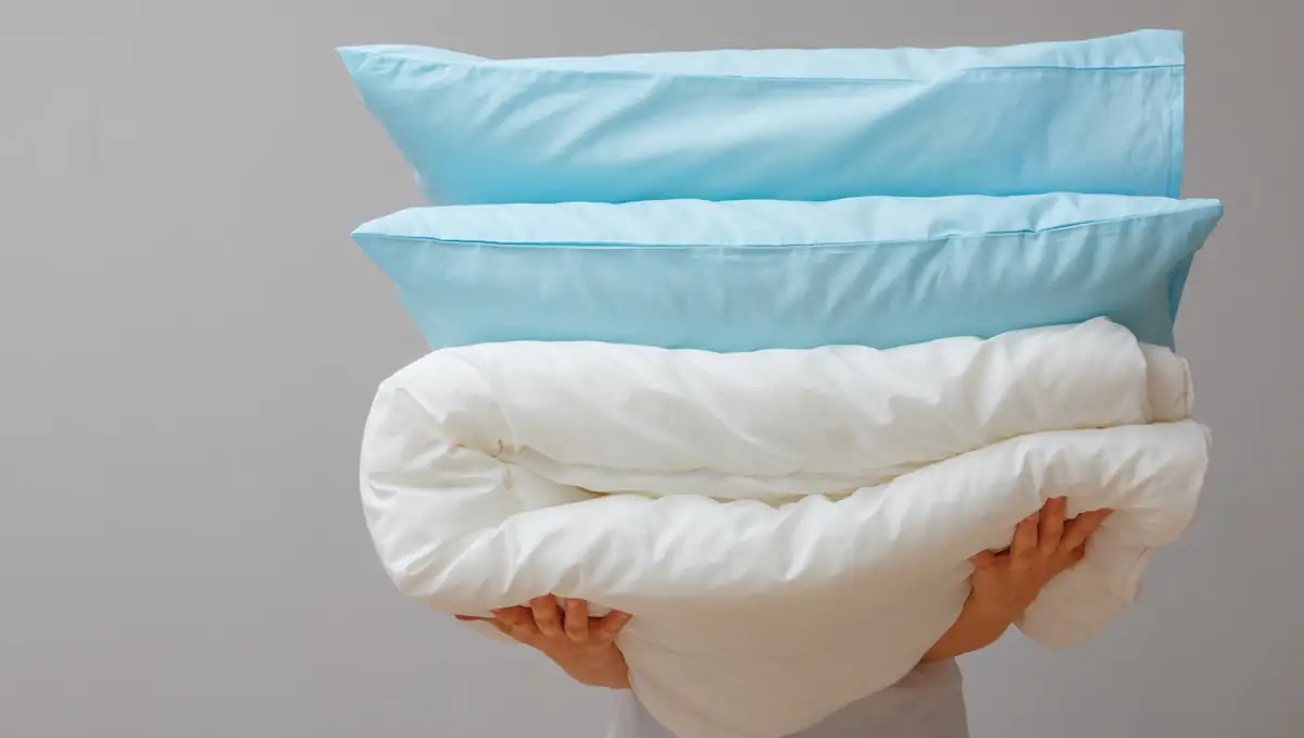 Bettwäsche: Person trägt gestapelte Kissen und Decke auf den Armen