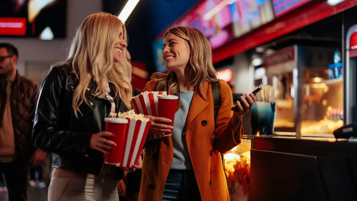 Zwei junge Frauen kaufen sich im Kino Popcorn und Getränke