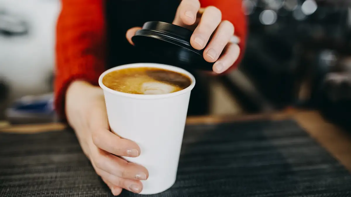 Coffe-to-go-Becher mit Kaffee, auf den eine Barista gerade einen Deckel setzt