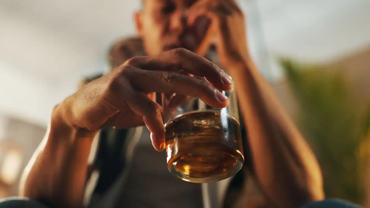 Alkoholiker sitzt mit einem Glas Whiskey und dem Kopf in den Händen