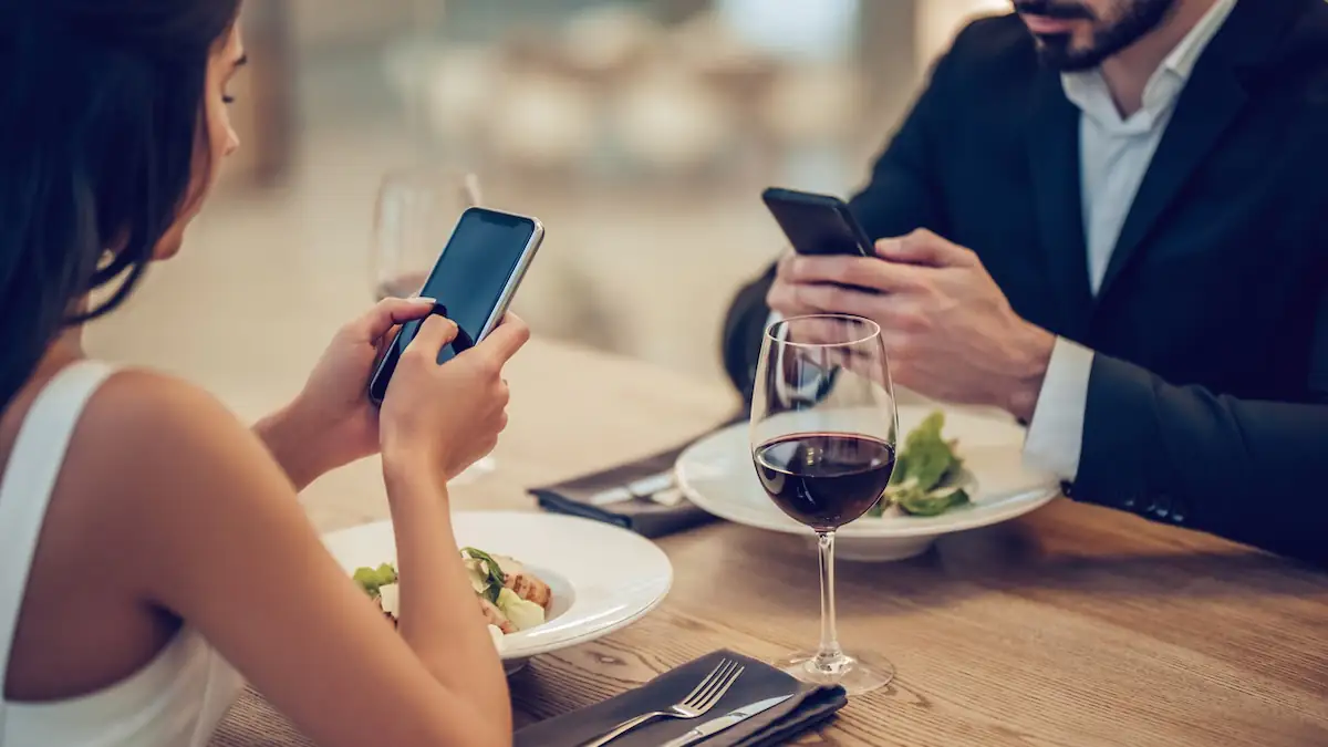 Paar sitzt im Restaurant, jeder ist mit seinem Smartphone beschäftigt