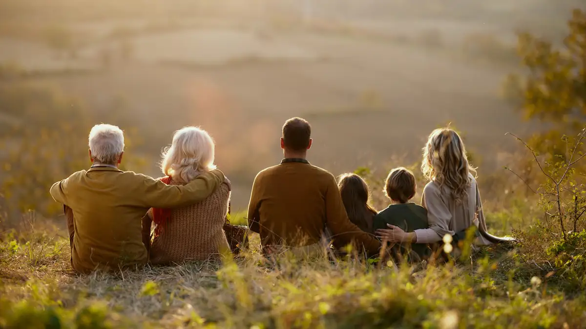 Alter Symbolbild: Familie mit drei Generationen sitzt zusammen im Grünen mit dem Rücken zur Kamera