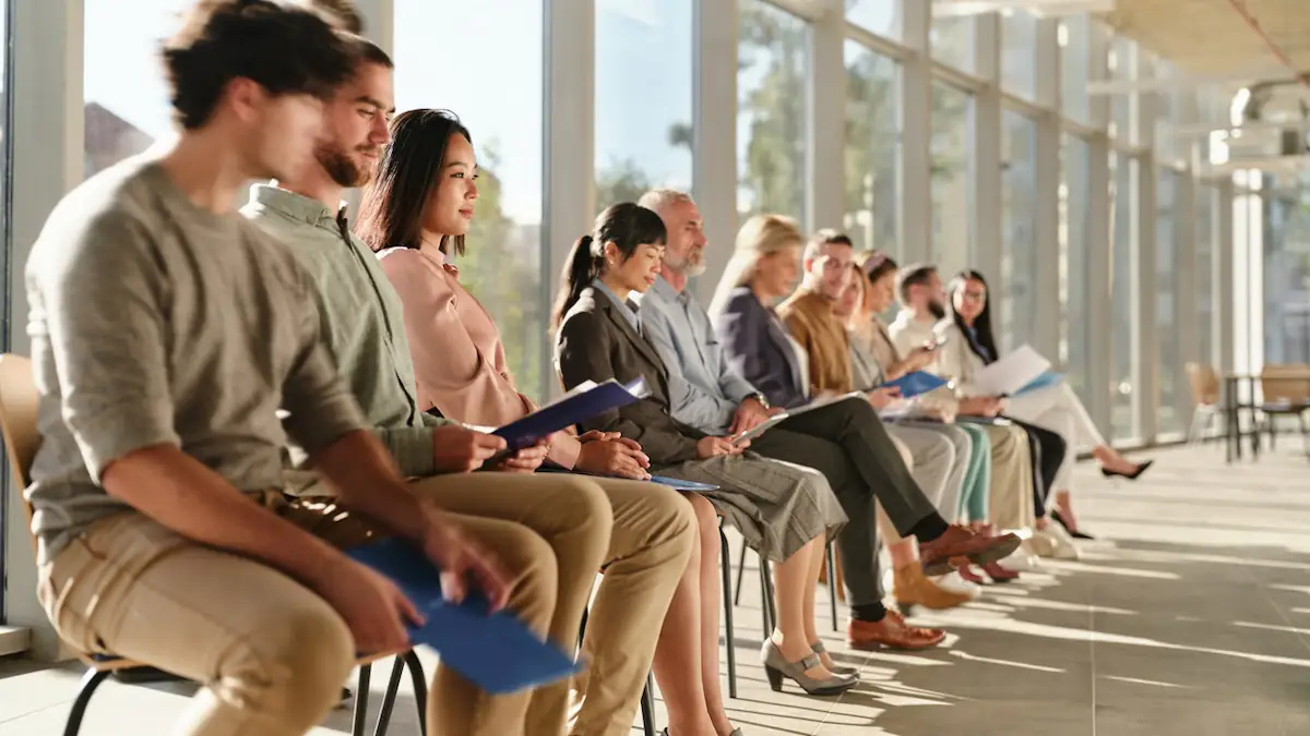 Apple-Bewerbungen: Eine Reihe von Bewerberinnen und Bewerber sitzen nebeneinander vor einem hellen Fenster