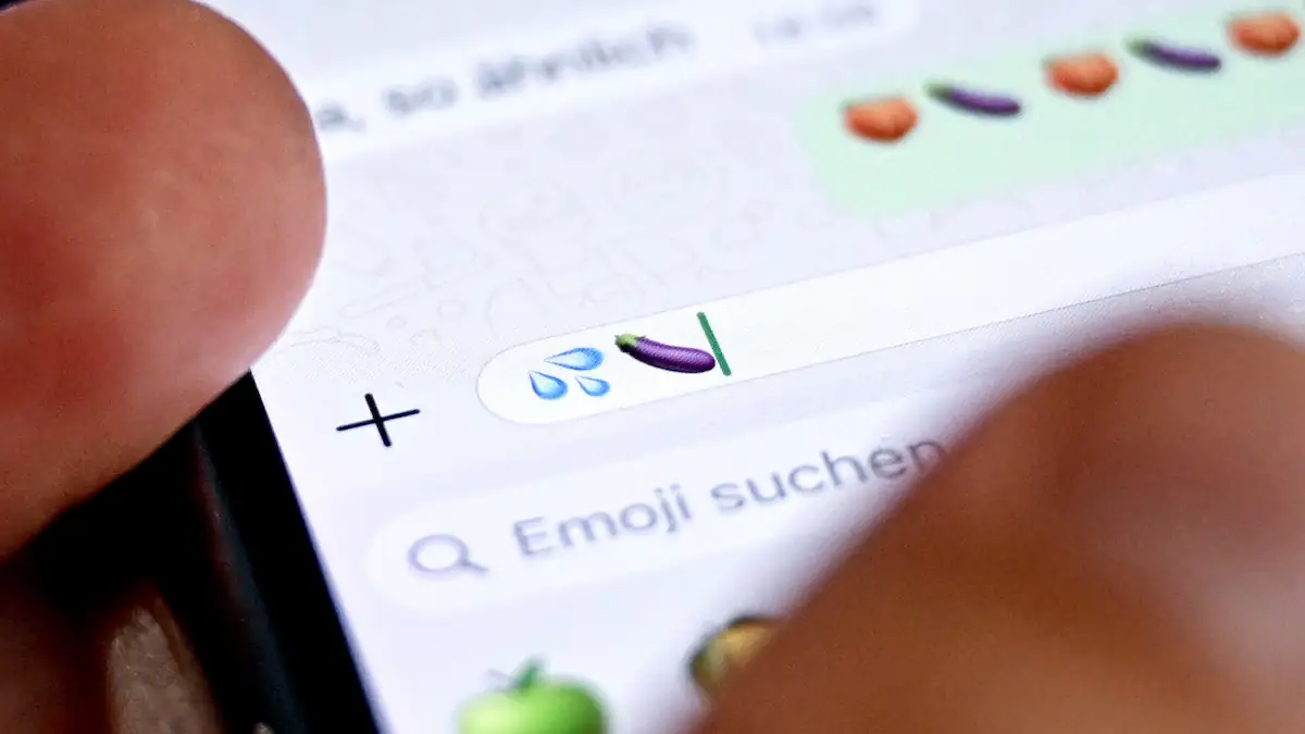 Jemand tippt auf einem Smartphone-Display in einen WhatsApp-Chat das Auberginen-Emoji