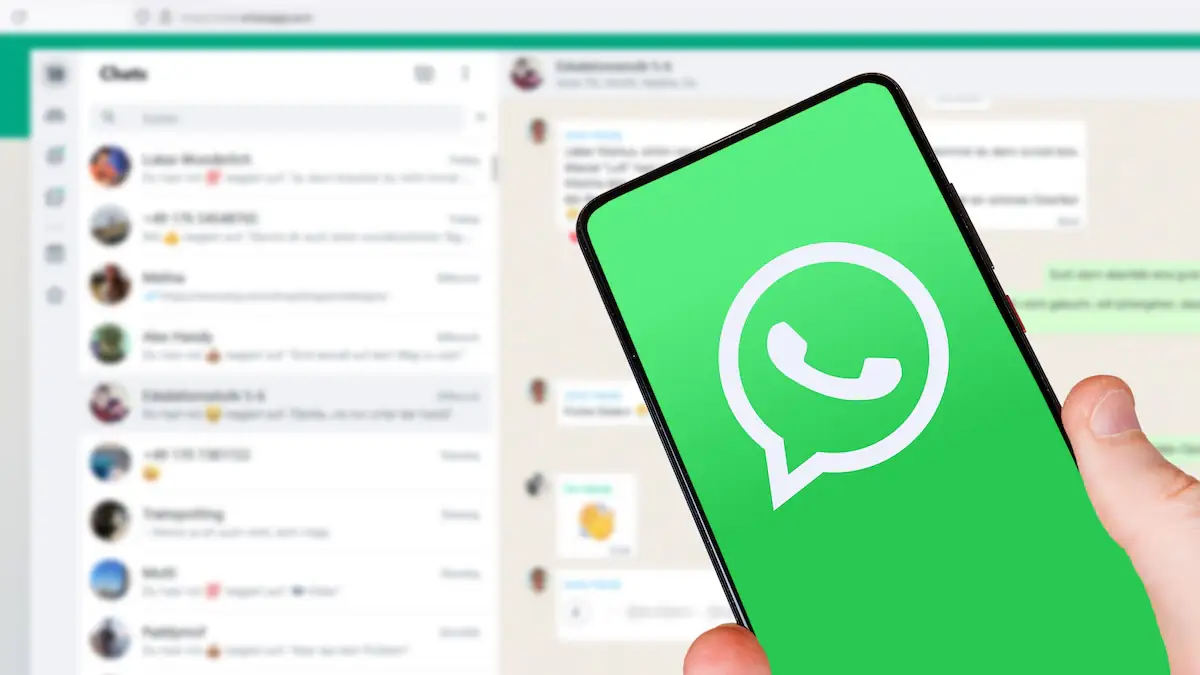 Smartphone mit WhatsApp wird vor einen verschwommenen Hintergrund gehalten, der WhatsApp Web zeigt