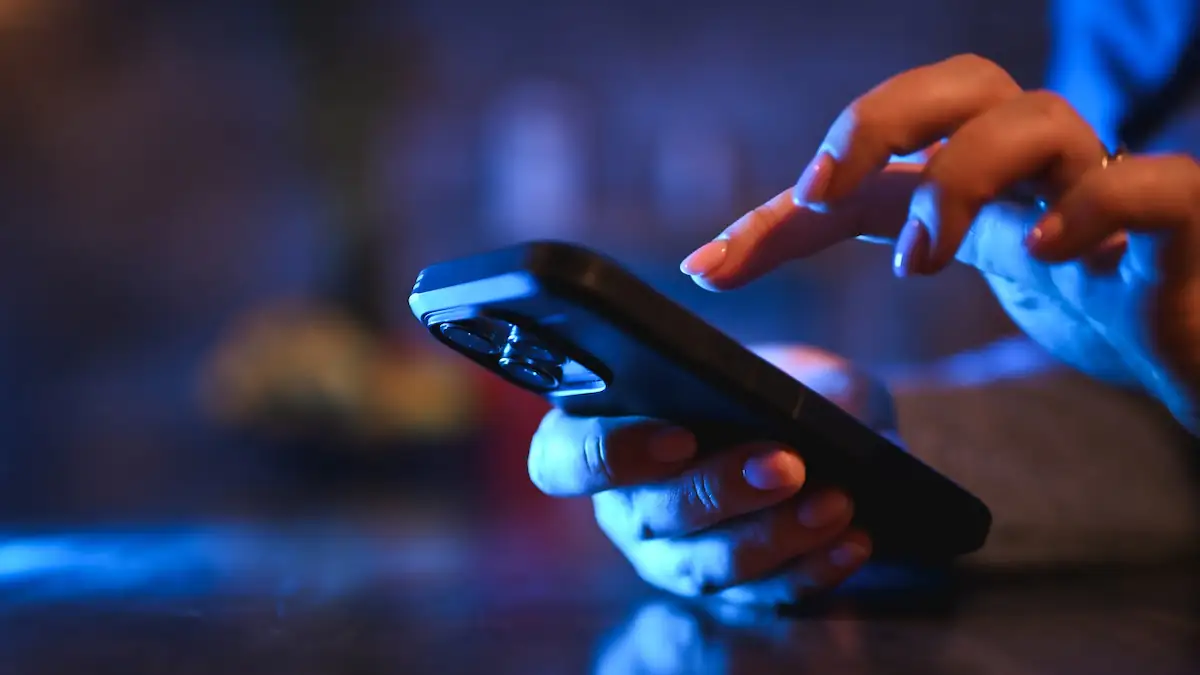 Malware-Apps: Jemand hält in rot-violettem Licht ein Smartphone in der Hand