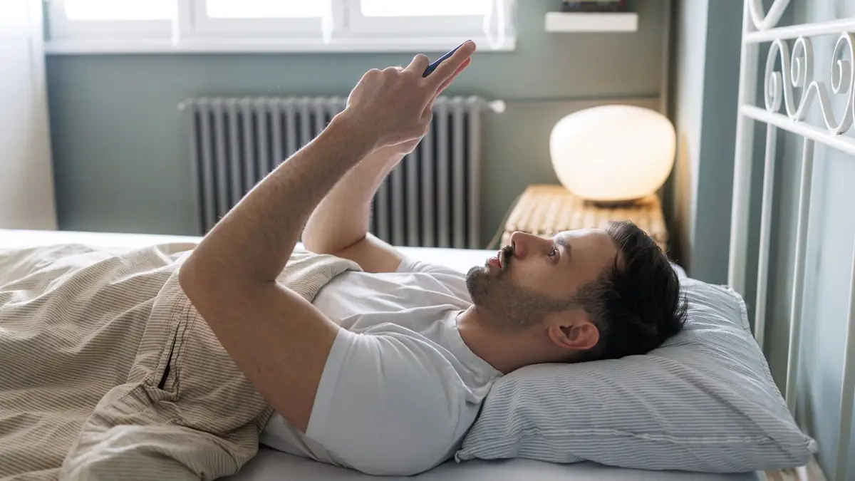 Bed Rotting: Mann liegt mit Handy tagsüber im Bett