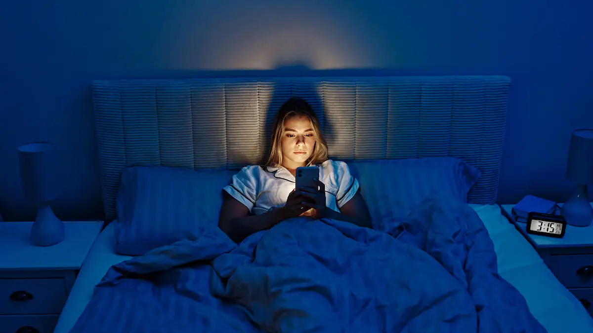 Bed Rotting: Frau liegt mit leuchtendem Handy nachts im Bett