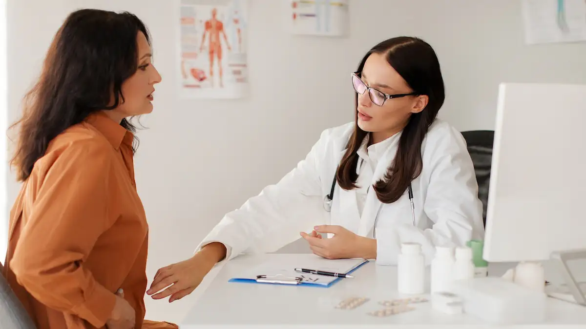 Gender Pain Gap: Frau sitzt mit Schmerzen einer Ärztin gegenüber