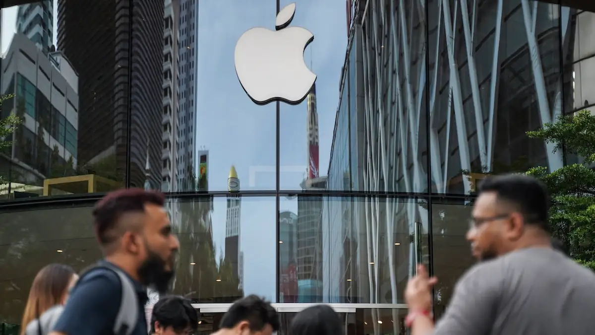 Apple-Logo an einer spiegelnden Glasfront, vor der Menschen laufen
