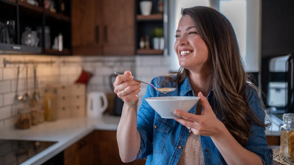 Frau isst lächelnd ein Gericht von einem Löffel