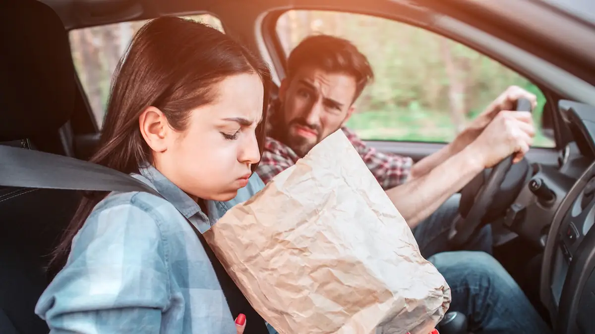 Hilft Petersilie gegen Reisekrankheit? Frau sitzt mit einer Papiertüte im Auto., weil ihr übel ist