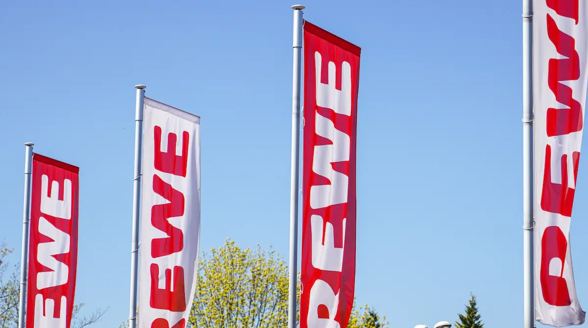 Rewe Rückruf: Logo des Supermarktes auf mehreren länglichen Fahnen