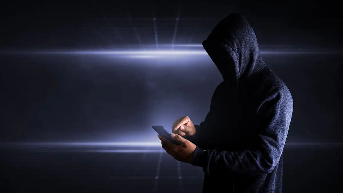 Kapuzengestalt hält Smartphone: Malware „Massiv“ schleust Trojaner über falsche Apps ein