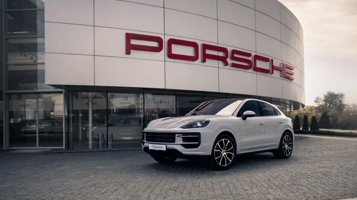 Ein weißes Auto steht vor dem Porsche Logo