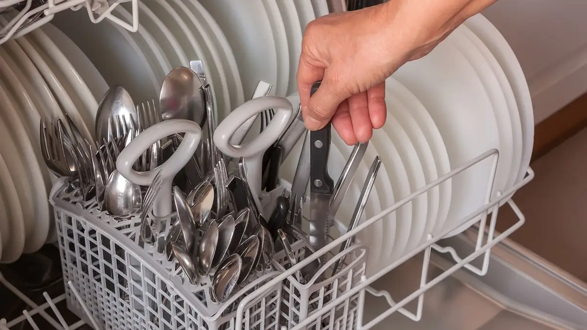 Jemand steckt ein Messer in den Besteckkorb in einem Geschirrspüler