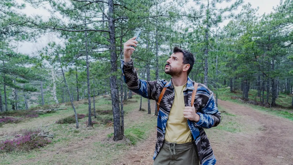 Mann hält beim Wandern sein Smartphone hoch, weil er schlechtes Handynetz hat