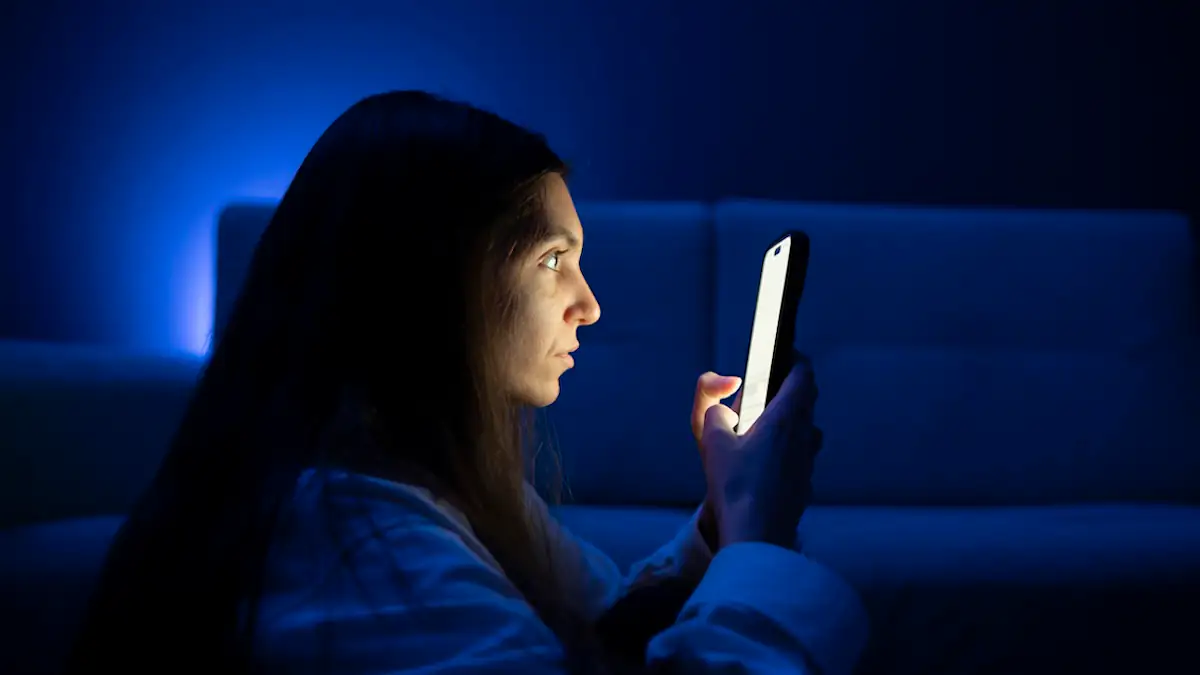 Falsche WhatsApp-Version im Umlauf: Frau schaut im Dunkeln auf ein leuchtendes Smartphone