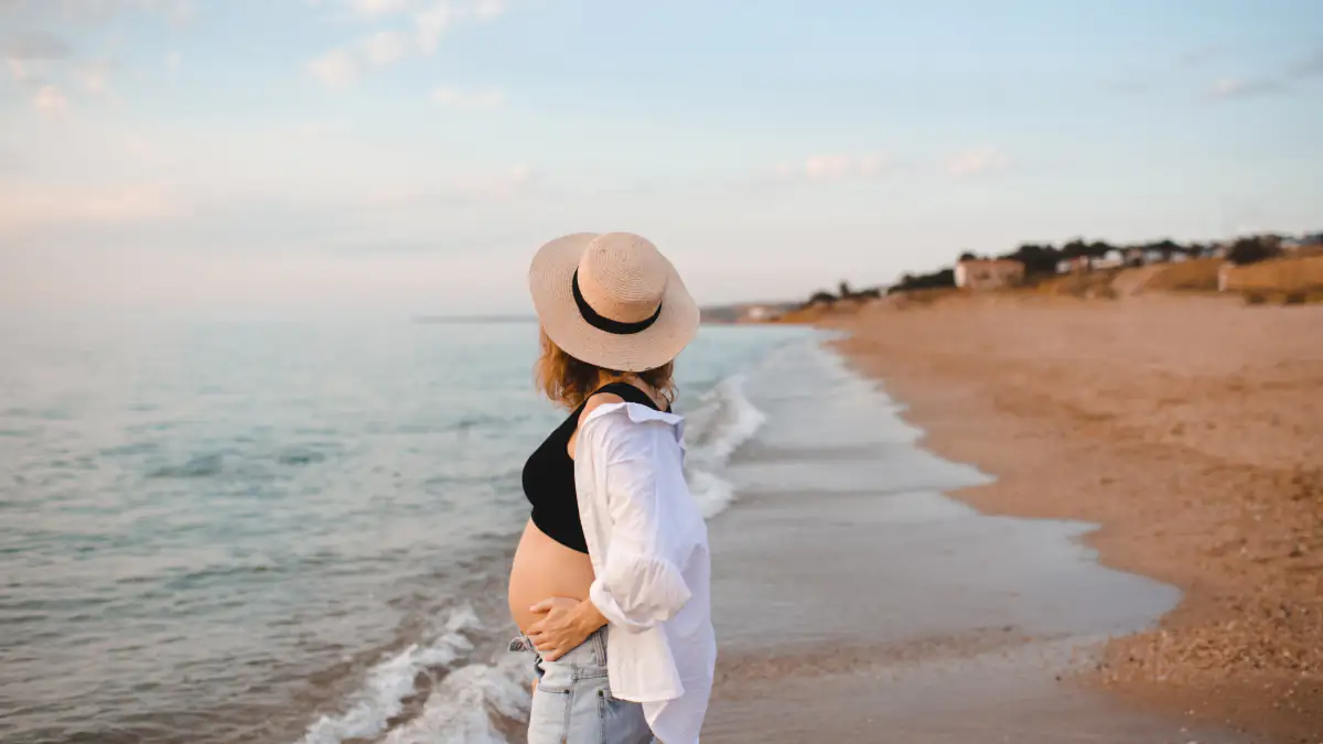 Symbolbild Babymoon-Trend: Schwangere Frau steht am Strand