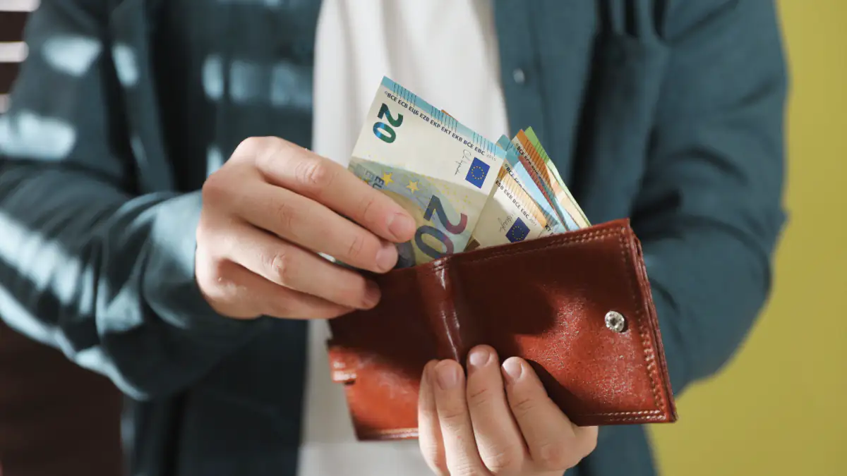 Person hält Euroscheine und eine Geldbörse in der Hand