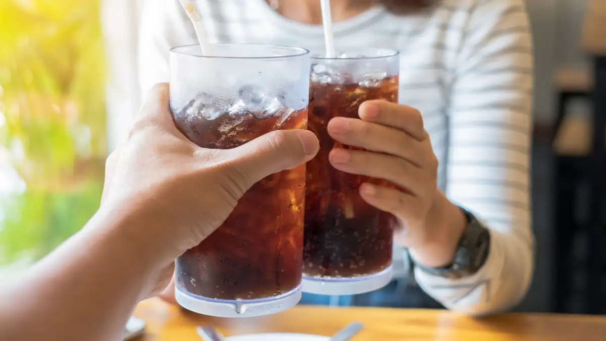 Zwei Personen stoßen mit Cola-Getränk in Gläsern an