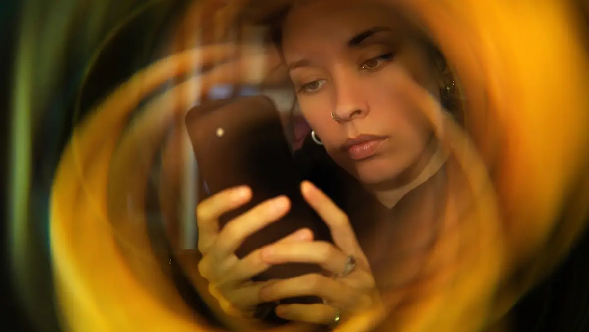 Vom Doomscrolling zum Doomjobbing: Junge Frau mit Smartphone, um die sich eine Spirale bildet