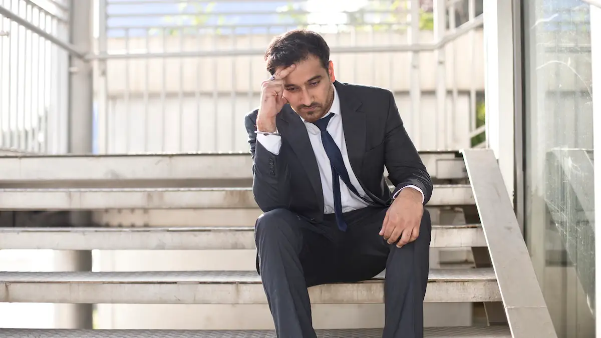 Doomjobbing: Frustrierter Büroangestellter im Anzug sitzt auf einer Treppe