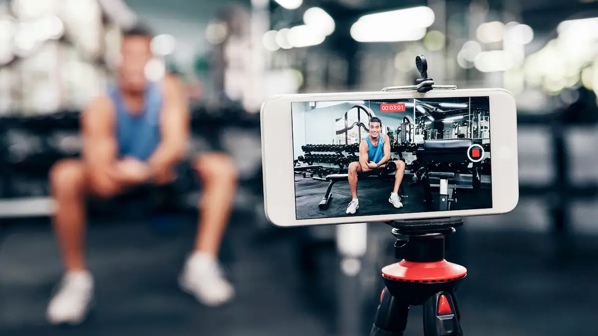 Looksmaxxing: Fitness-Influencer nimmt im Fitnessstudio ein Video mit dem Smartphone von sich auf