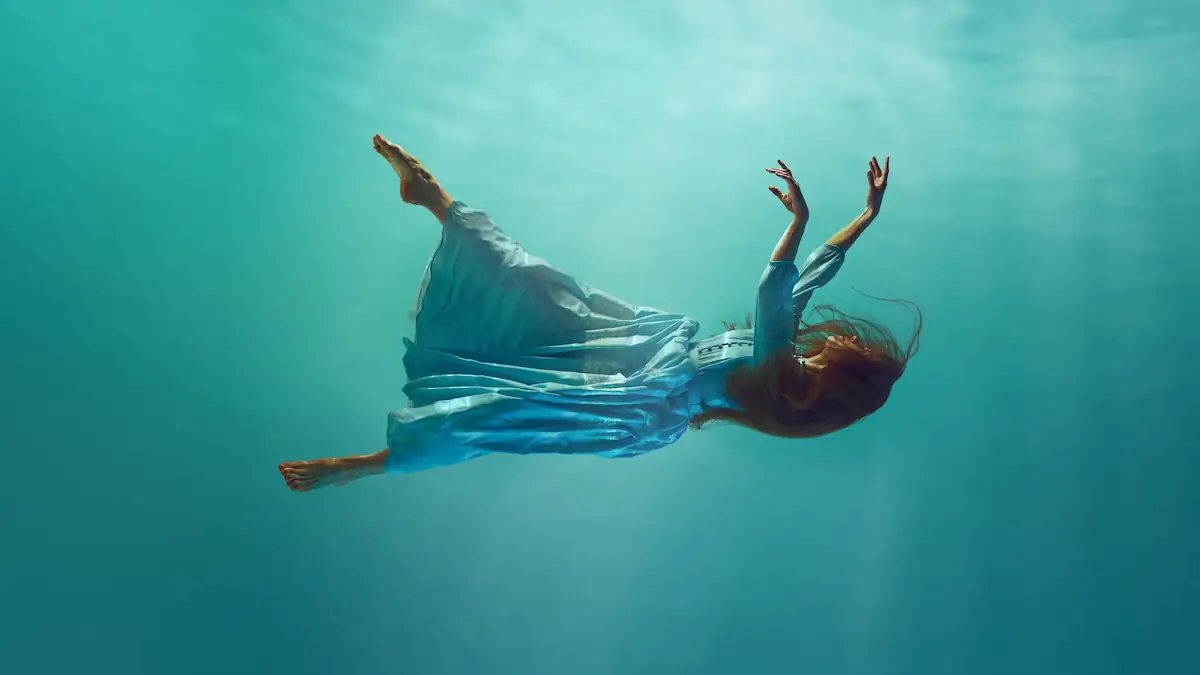 Nahtoderfahrung Symbolbild: Junge Frau treibt in einem Kleid schwerelos unter Wasser