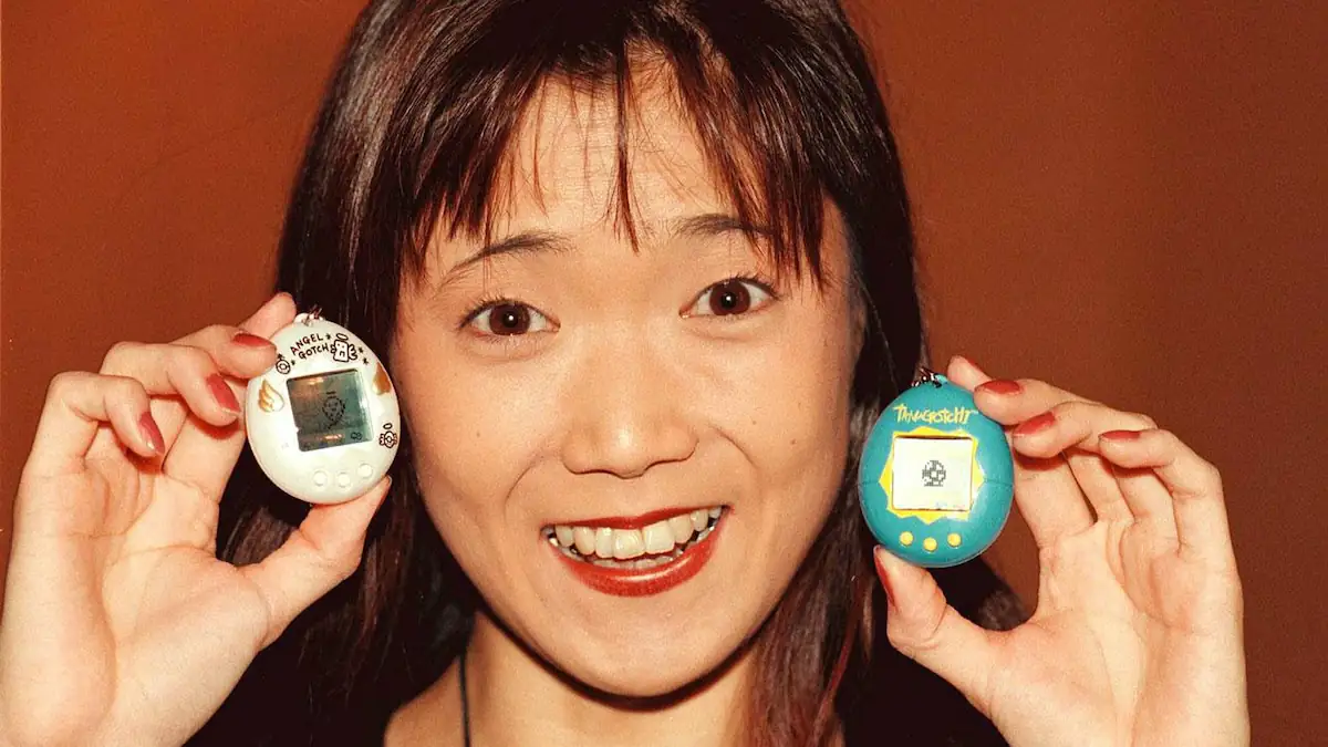 Tamagotchi-Erfinderin Aki Maita hält zwei der Geräte neben ihr Gesicht