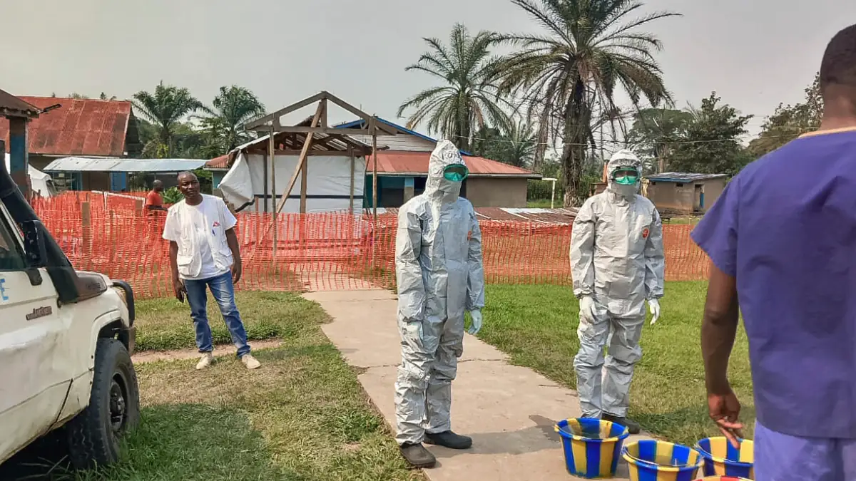 Vermummte Personen stehen auf einem Weg vor Palmen und schützen sich gegen Ebola
