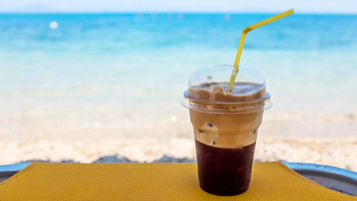 Dirty Soda in einem durchsichtigen Plastikbecher, da vor einer Strand-Kulisse mit Meerblick steht